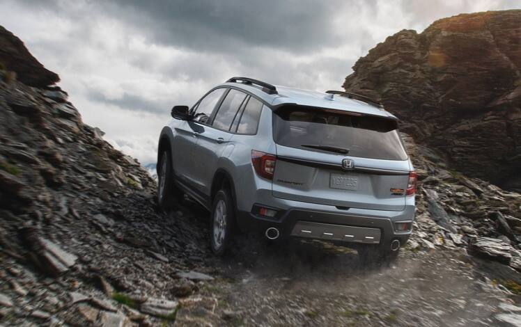 Rear three-quarter driver-side view of the 2023 Honda Passport TrailSport in Sonic Gray Pearl driving up a rocky outcrop. 